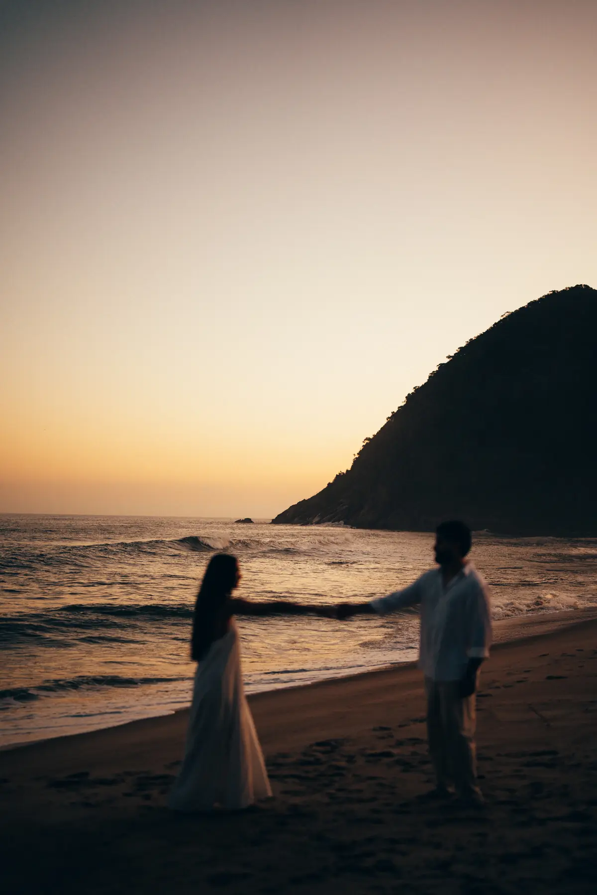 Nós dois de mãos dadas na beira do mar, ao pôr do sol
